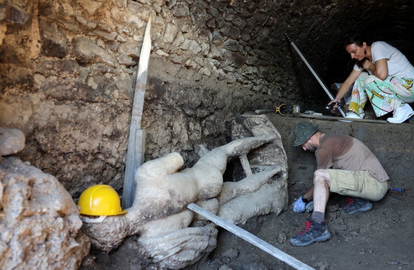 Archaeologists stand next to a marble statue, uncovered at the site of the remains of the ancient city of Heraclea Sinitica