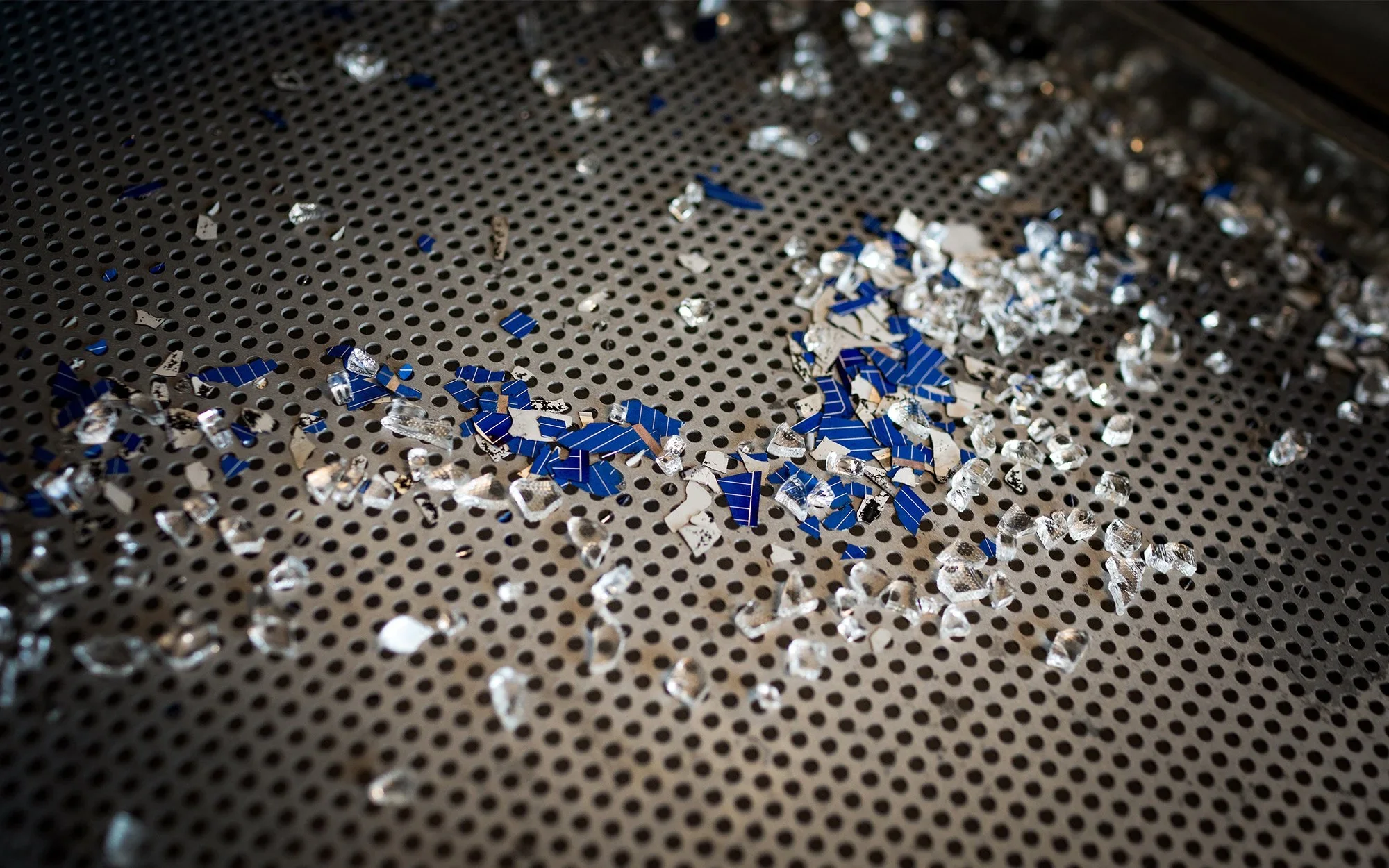 Broken pieces of clear glass and blue silicon on a perforated metal trayBits of silicon and glass are separated from the rest of the panel.