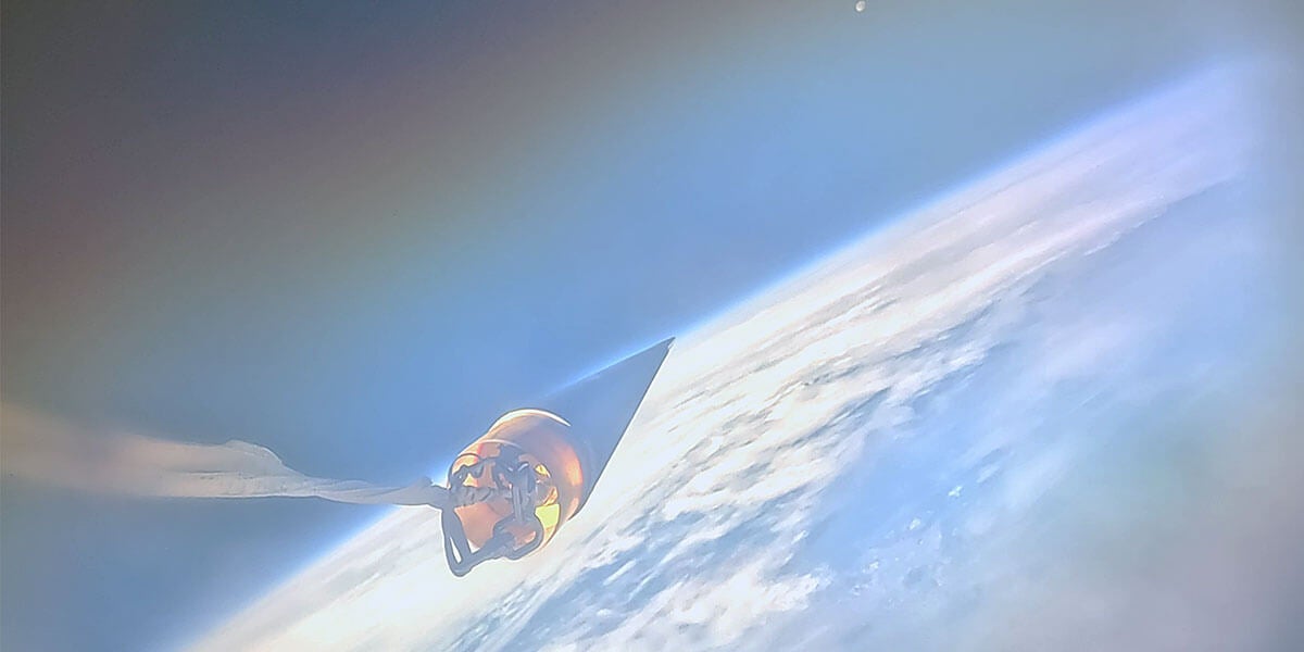 Photo from space. The nose cone of USCRPL’s rocket points towards the moon, across Earth’s horizon.