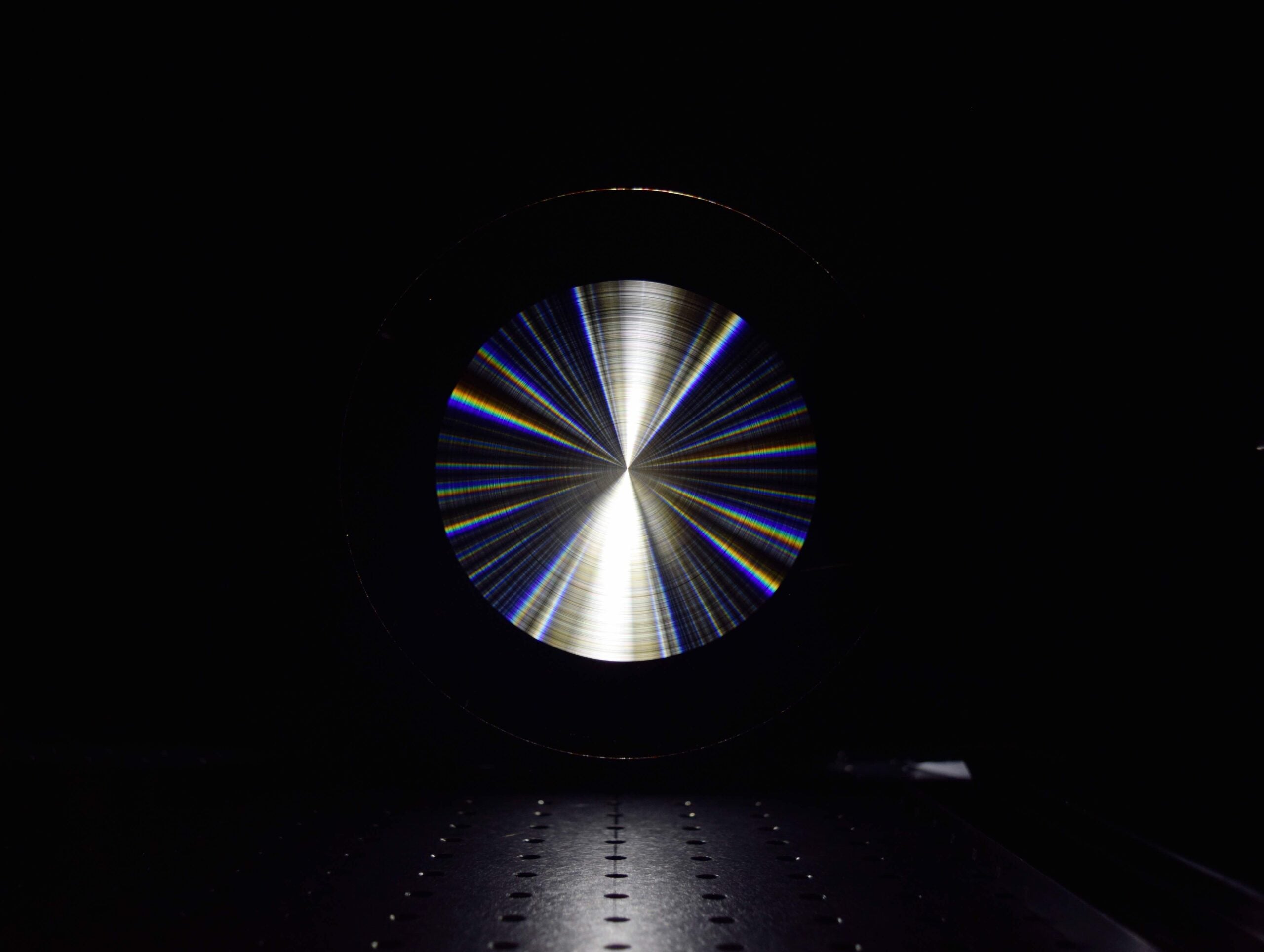 The concentric rings of microscopic indentations on the researchers’ flat lens are optimized to bring all wavelengths of light into focus at the same time.