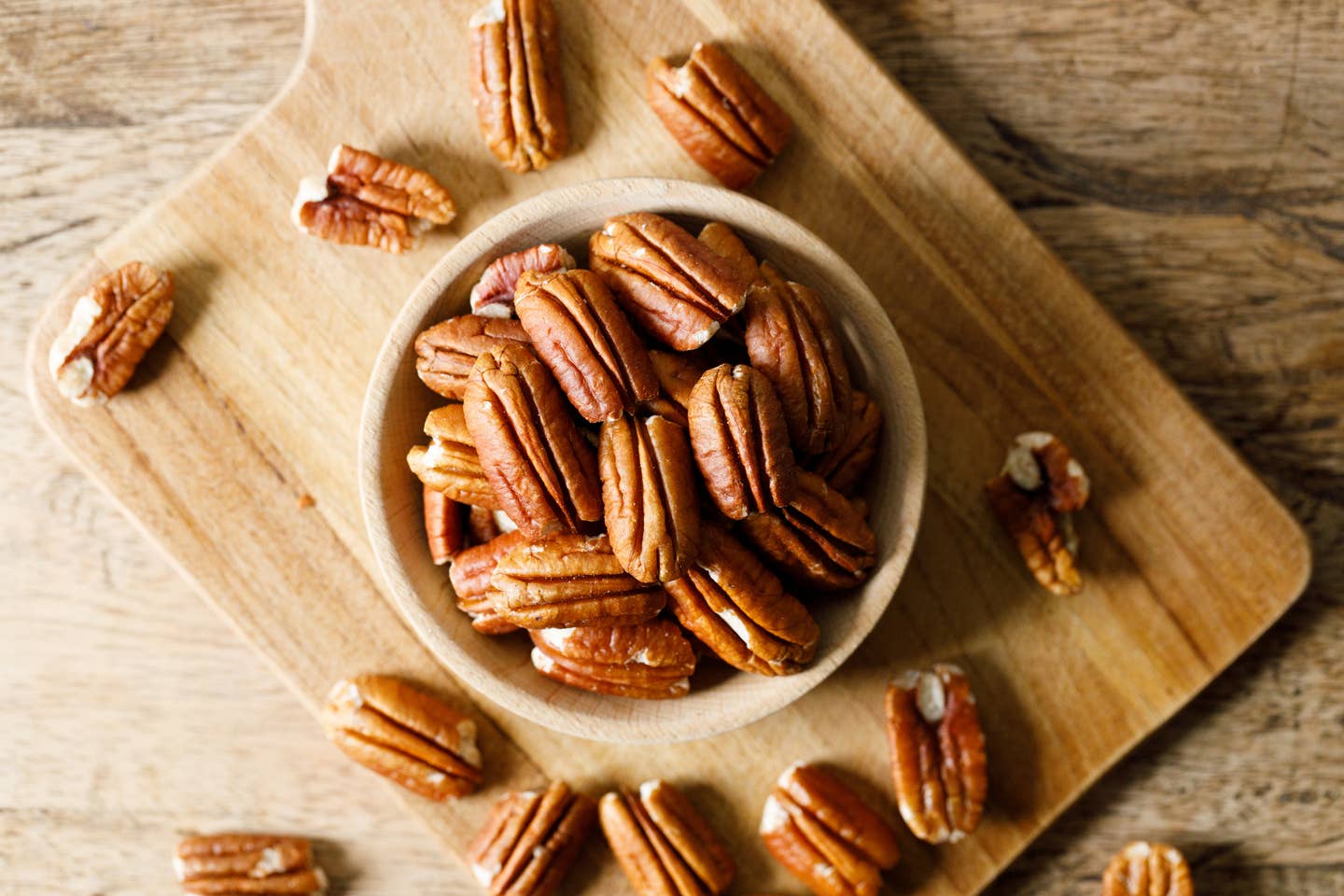 Pecan nuts on rustic wooden table in a wooden bowl.