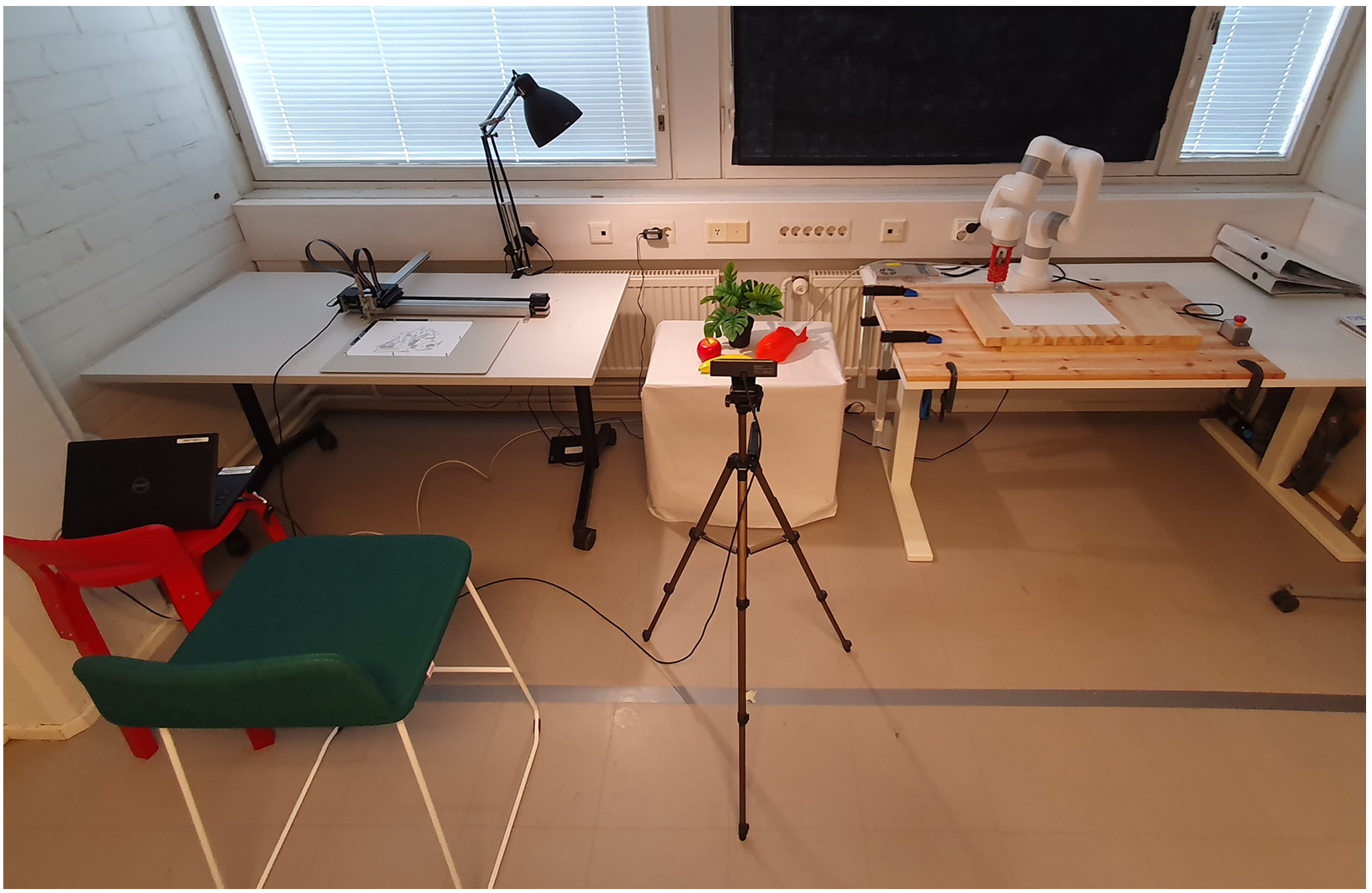 Experimental setup including the robots (AxiDraw, left; xArm), arrangement, camera and participant chair. Missing from the picture is the folding screen, which was initially used to keep the robots out of sight.