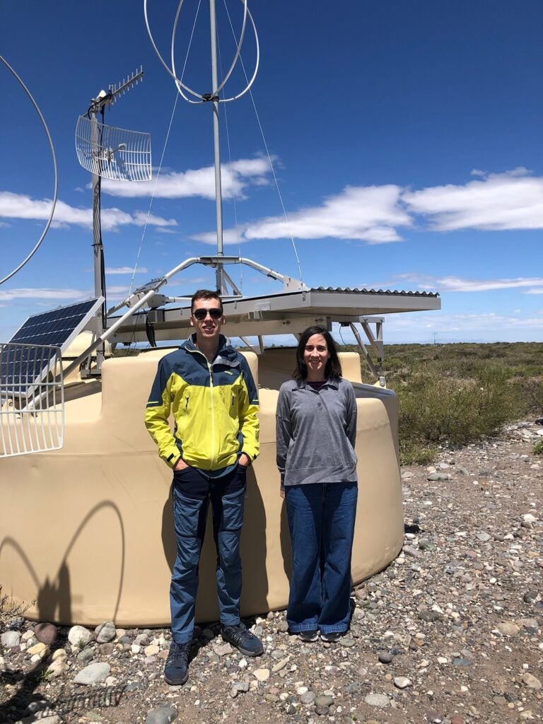 Domenik Ehlert and Foteini Oikonomou in front of one of the 1,600 surface detectors that are part of the Pierre Auger Ultra-high Energy Cosmic Ray Observatory in Malargüe, Argentina.