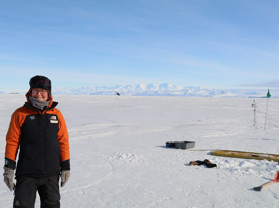 Maren Richter on the fast ice next to a measurement site from which a sea ice core was taken. Coring equipment and part of the automated measuring site is on the right. The Trans-Antarctic Mountains are visible in the background.