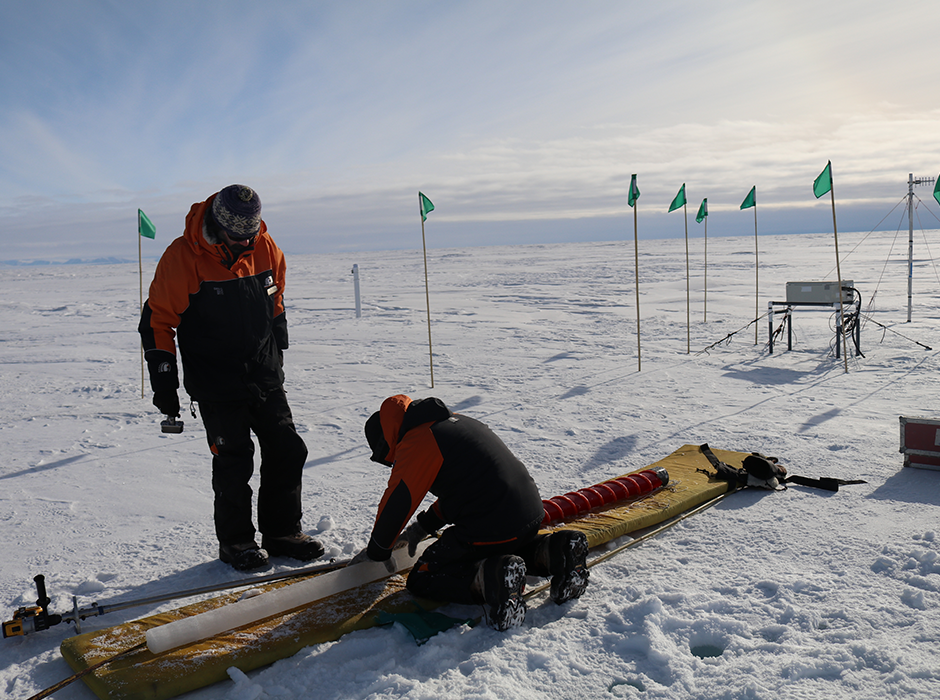 Maren Richter (kneeling) pieces together a sea ice core taken at an automated measuring station (seen on the right). Professor Lars Smedsrud, of the University of Bergen, is seen standing.