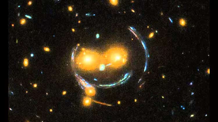 The light from distant objects passed through the gravitational field of closer galaxies to create a gravitational lens that looks like a "smiley face" to the Hubble Space Telescope.