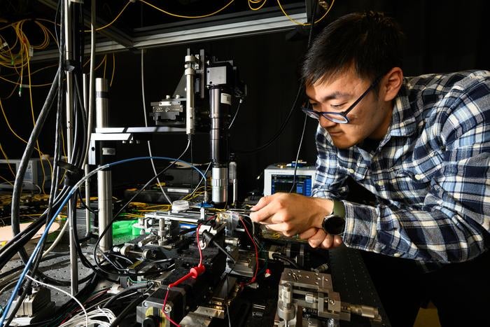 Electrical and computer engineering PhD student Shixin Xue ’20 MS (optics) connects the thin film lithium niobate laser device to a commercially available semiconductor chip, optical fiber, and probe that applies an electrical signal.

