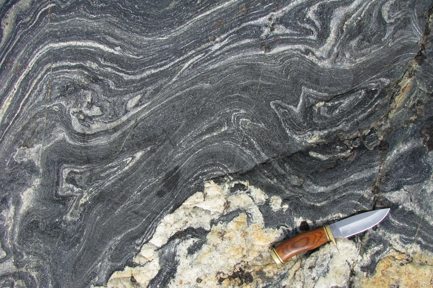 A cluster of ancient rocks estimated to be 4.16 billion years old rises from the Nuvvuagittuq Greenstone Belt in northeastern Canada, with a knife placed beside them for scale.