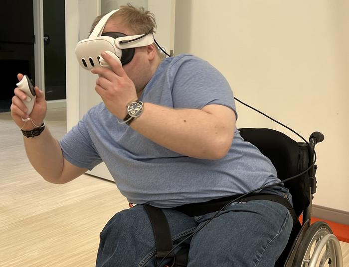 A person in a wheelchair wearing VR googles holding a controller leaning to avoid hazards in the VR game, Beat Saber