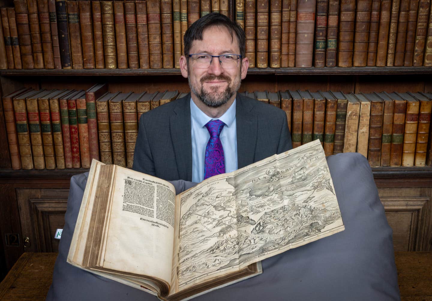 Professor Nathan MacDonald with Christopher Froschauer's 1525 Old Testament open at Lucas Cranach the Elder’s map of the Holy Land, in the Wren Library, Trinity College, Cambridge.