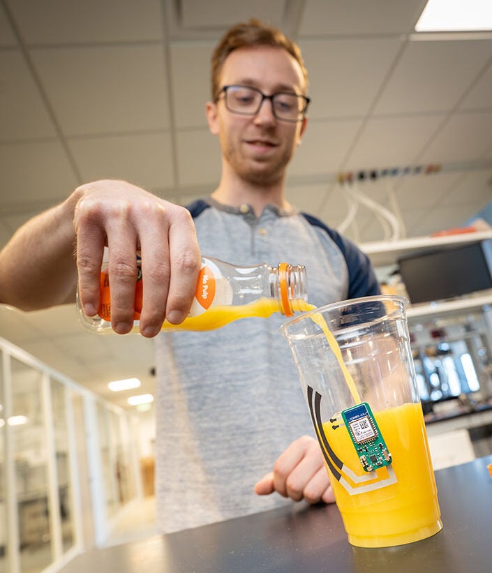Ryan Burns, a Ph.D. student in electrical and computer engineering at UC San Diego’s Jacobs School of Engineering, demonstrates the sticker by placing it on a cup of orange juice.