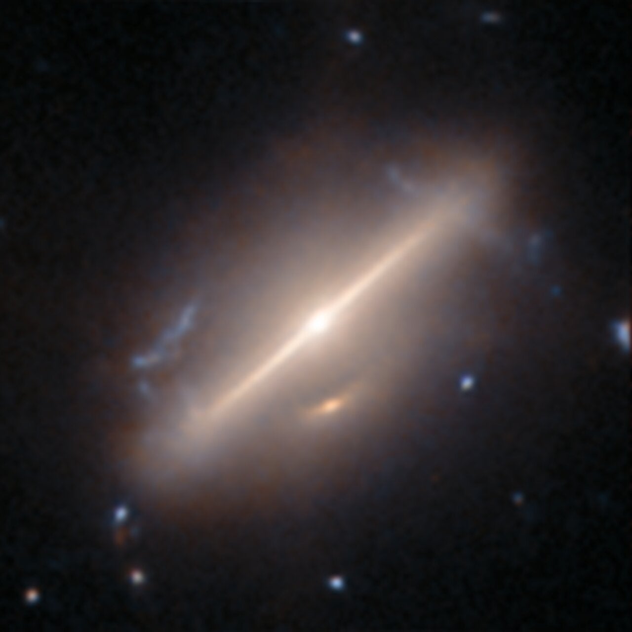 This oval-shaped galaxy is perhaps most striking for the long, thin beam of light stretching across its centre. This is thought to be the result of a galaxy merger. A less conspicuous feature is the small arc of light just below the galaxy’s core. This is thought to be the secondary galaxy in the merger, or a potential image formed by gravitational lensing, where the mass of the foreground galaxy has bent light from a distant galaxy behind it to create the small arc of light.