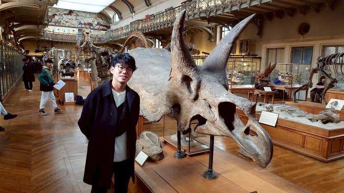 Seishiro Tada (left) standing next to an awe-inspiring Triceratops skull, with its enormous nasal cavity visible at the front.