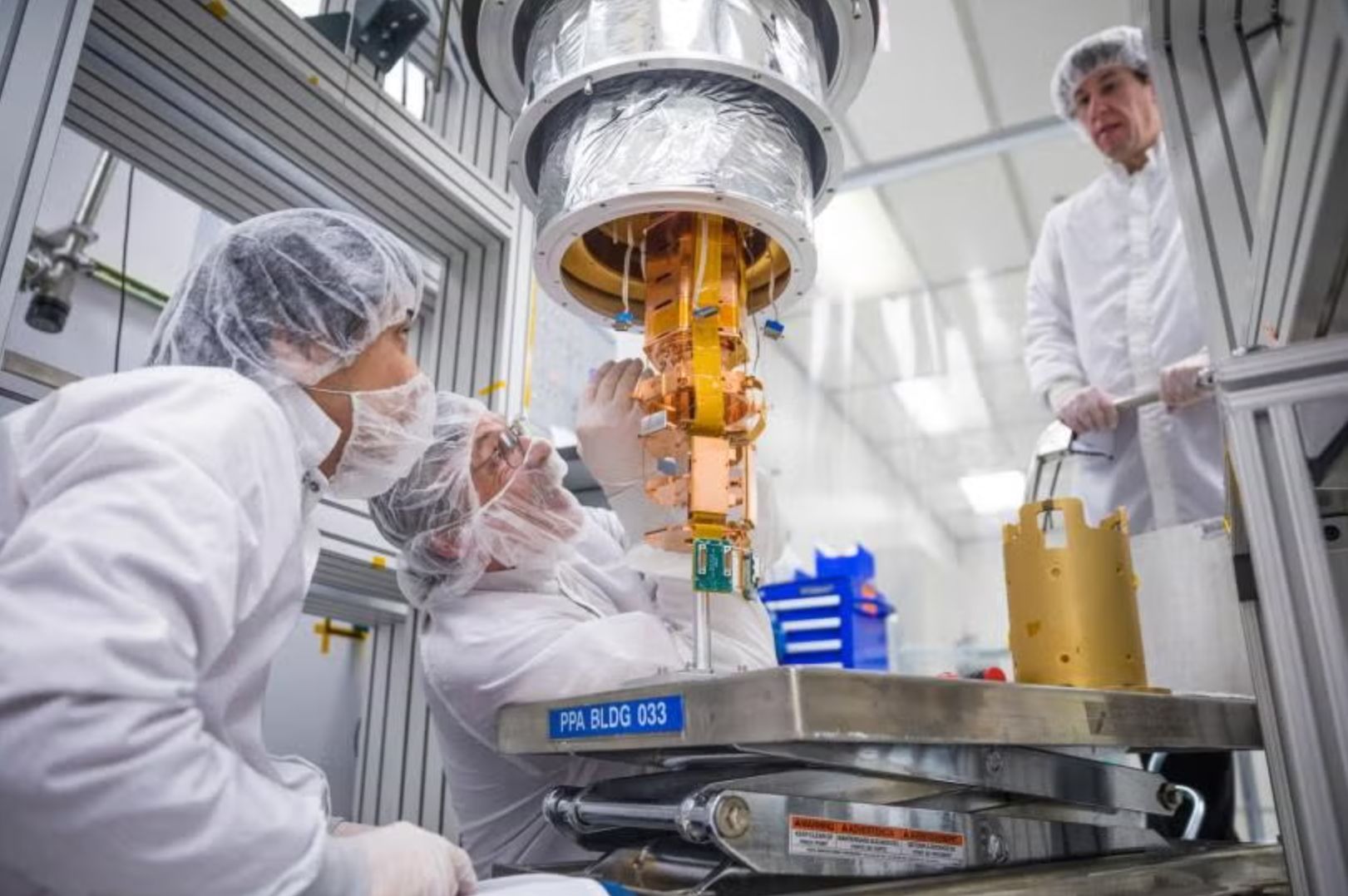 SLAC scientists and a technician inspect a SuperCDMS detector tower installed at the bottom of the dilution refrigerator used for tower testing. 