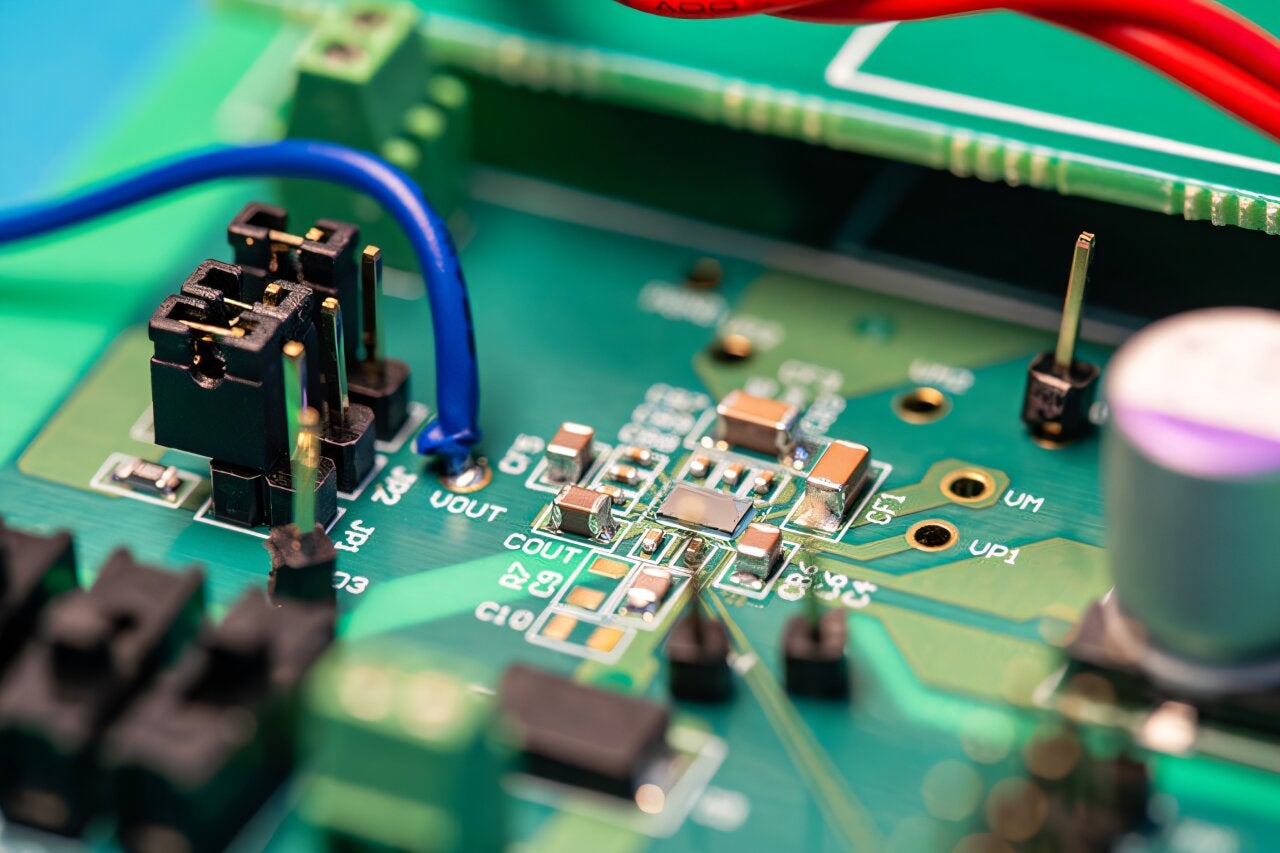 The printed circuit board used to test the new DC-DC step-down conversion chip, shown in the center, surrounded by capacitors. The piezoelectric resonator is mounted underneath the circuit board and electrically connected to the chip. 
