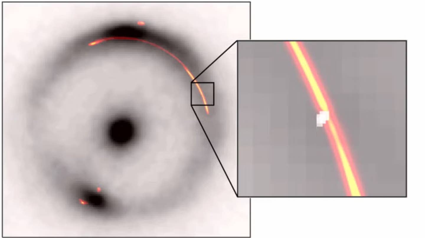 The gravitational lens system JVAS B1938+666. The black ring and central dot show an infrared image of a distant galaxy distorted by gravitational lensing. The orange emission shows radio waves from the same system. The inset highlights a small "pinch" in the image caused by an additional dense object—about a million times the mass of the sun—shown as a white blob.