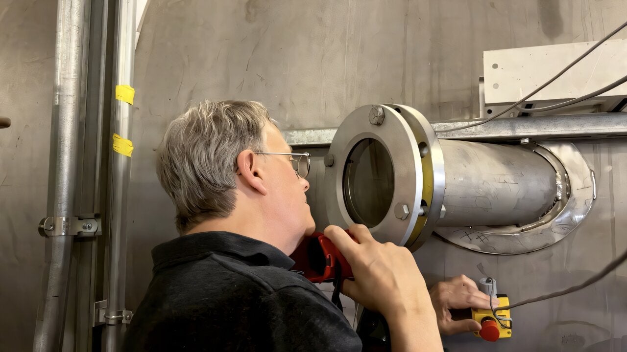 JPL senior research scientist James Polk peers into the condensable metal propellant (CoMeT) vacuum facility at JPL’s Electric Propulsion Lab, where a high-power electric thruster prototype his team developed was being put to the test in February 2026. 