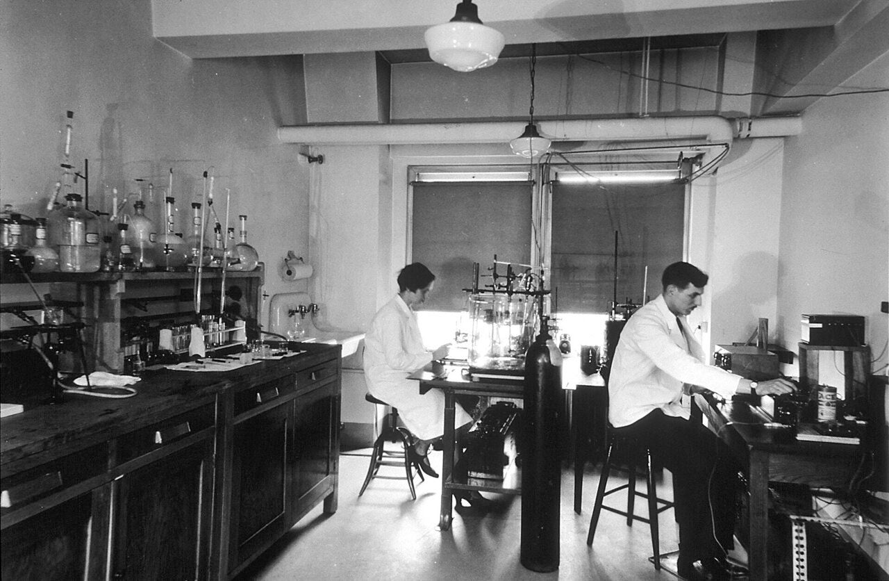Two scientists sitting on stools in an interior wide shot of Chemical Laboratory, part of the Central Cancer Research laboratories.