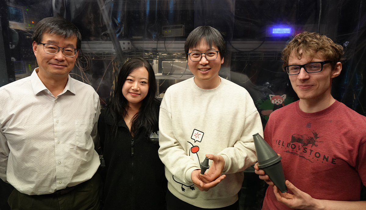 Jun Ye (left), a physicist at NIST and JILA, poses with members of his team (left to right) Zoey Hu, Dahyeon Lee and Ben Lewis, who are holding replicas of an optical laser cavity.