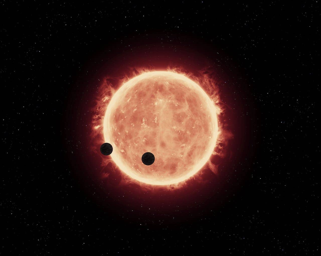 This artist's impression shows two Earth-sized worlds passing in front of their parent red dwarf star, which is much smaller and cooler than our Sun.