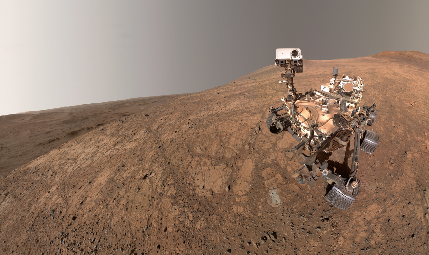 NASA’s Perseverance took this selfie at “Witch Hazel Hill” on Jezero Crater’s rim on May 10, 2025. The small dark hole in the rock in front of the rover is the borehole made when the rover collected the “Bell Island” sample. The small puff of dust left of center and below the horizon line is a dust devil.