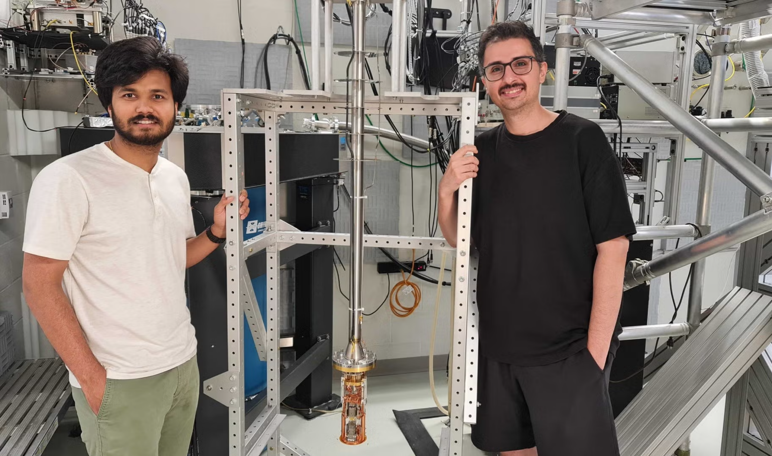 Sahand Tabatabaei and Pritam Priyadarsi, both PhD candidates, stand next to a low temperature scanning force microscope, the instrument that was used for taking experiment measurements.  