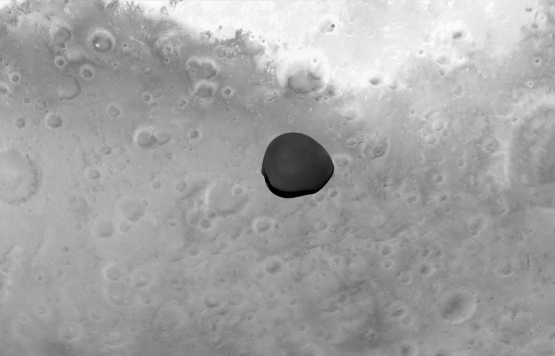 Martian moon Deimos appears dark, framed by the brighter planet Mars behind it, in this visible light monochromatic Asteroid Framing Camera image, acquired by ESA’s Hera spacecraft during its gravity-assist flyby on 12 March 2025.