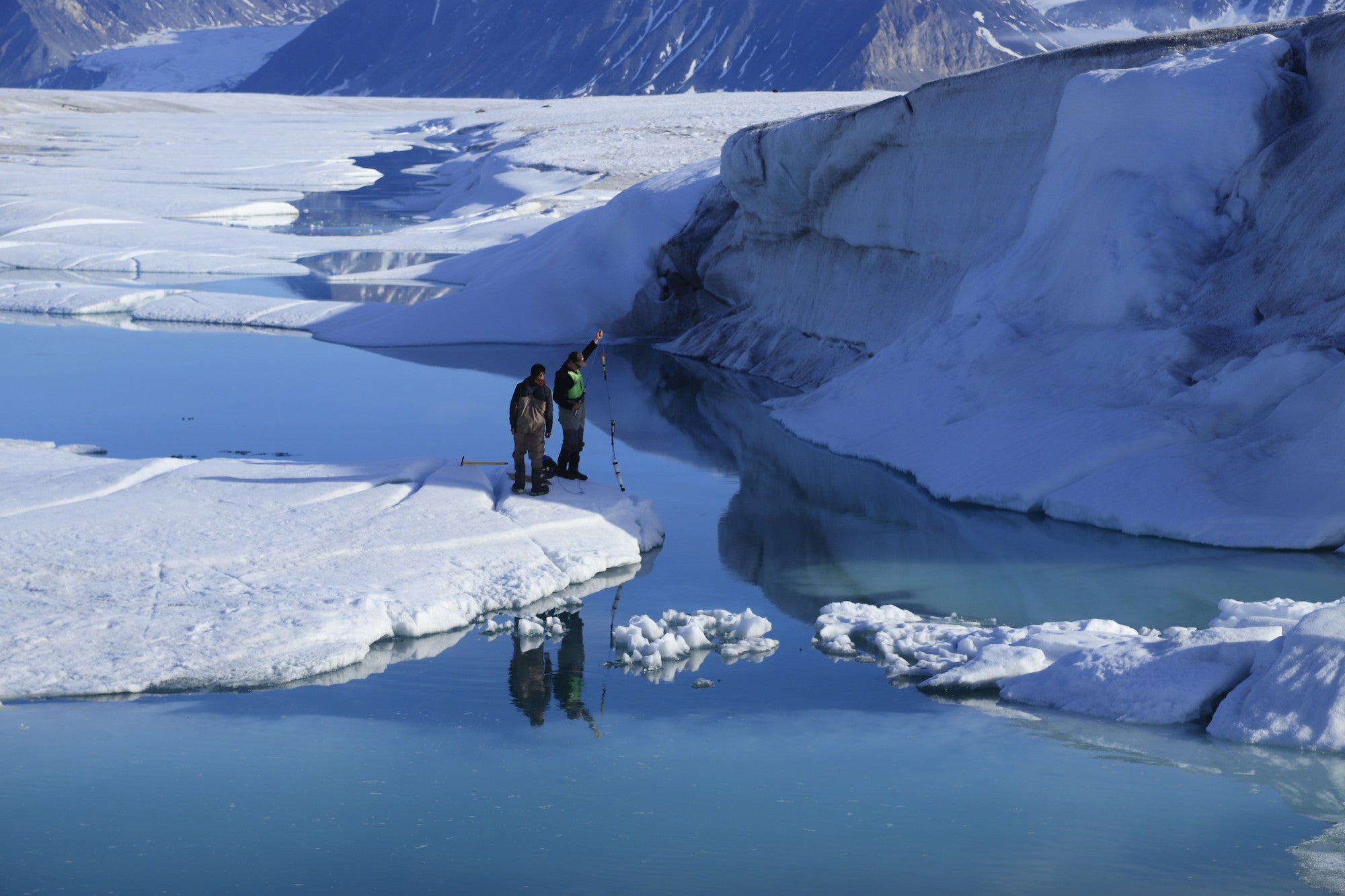 Researchers Joseph Shoapik and Jérémie Bonneau lower instruments through cracks in the ice shelf to measure temperature and salinity at different depths in the water below. 
