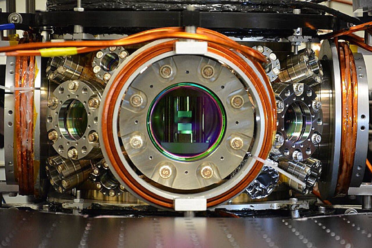 Quantum-optical spin glass apparatus: The curved mirrors (green-tinted cylinders at center) form an optical cavity to trap photons inside a stainless-steel vacuum chamber. The windows allow lasers to create and trap quantum gases (not present in this photo) between the mirrors.