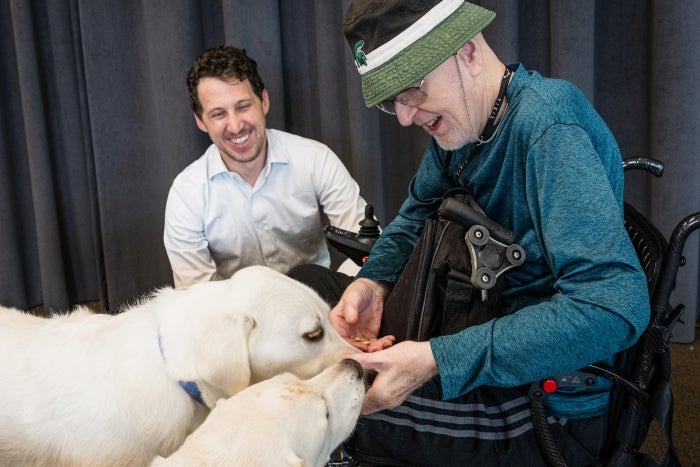 Retired attorney D. P. Stoller (right) treats Juno and Homer, the dogs of ASU Professor Noah Snyder-Mackler (left), whose research explores why larger dogs age faster and die younger, offering clues to human aging. 