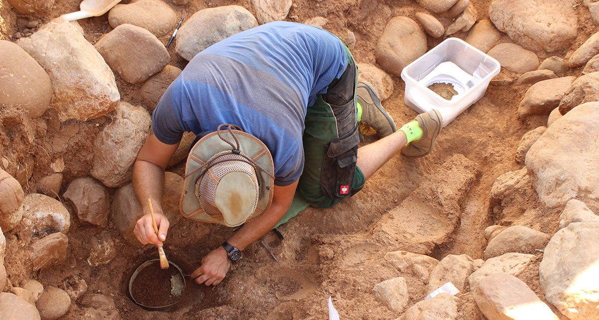 A student from the University of Basel unearthing a bronze ribbed bowl from the male grave “Est 11.” Next to his legs, The sword is still buried underground. 